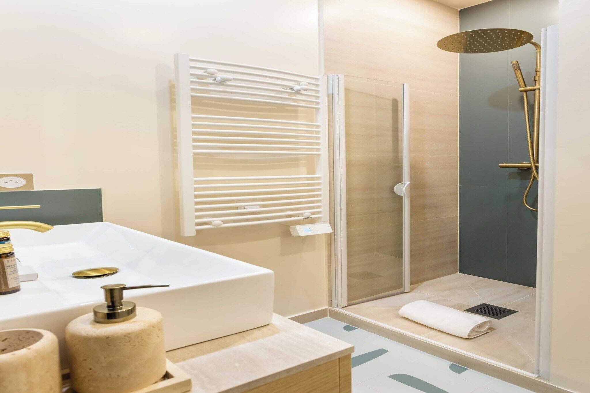 Ein modernes Badezimmer mit einem großen weißen Waschbecken, einer Dusche mit Glastrennwand und einem goldfarbenen Duschkopf sowie einem Handtuchhalter.