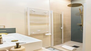 A modern bathroom with a large white sink, a glass-enclosed shower with a gold showerhead, and a towel rack.
