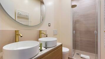 A bathroom with two sinks, a mirror, a toilet, and a shower.