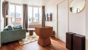 A modern living room with a sofa, a round ottoman, and a flat-screen TV. - Port-Royal Residence - Chic apartment - 2BR-4P (Paris)