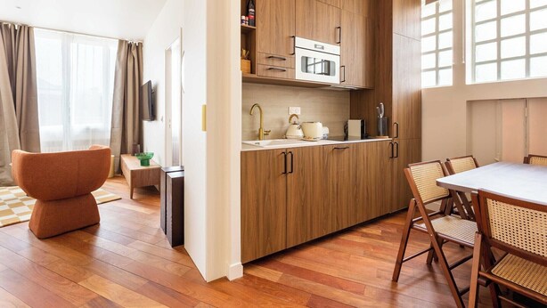 A modern kitchen with wooden cabinets, a microwave, and a sink. There is a dining area with a table and chairs. - Port-Royal Residence - Chic apartment - 2BR-4P (Paris)