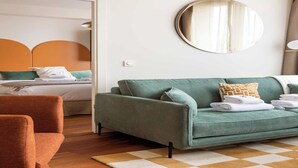 A modern hotel room with a green sofa, a wooden floor, a checkered rug, and a bed with a white headboard. - Port-Royal Residence - Chic apartment - 2BR-4P (Paris)