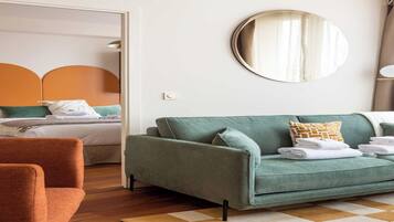 A modern hotel room with a green sofa, a wooden floor, a checkered rug, and a bed with a white headboard.