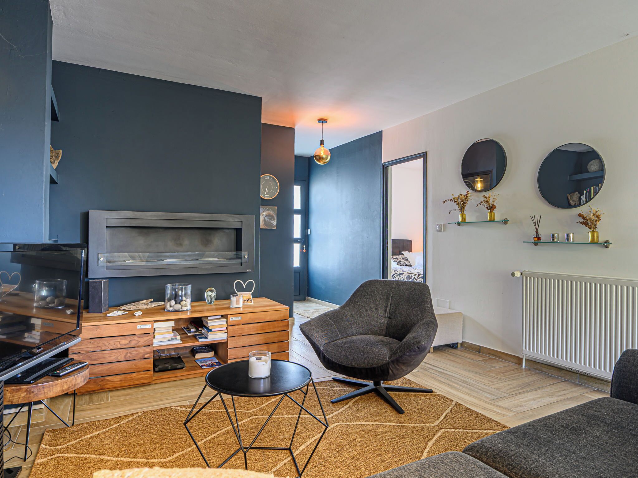 Una sala de estar moderna con televisor de pantalla plana, mueble de almacenamiento de madera, asientos cómodos y elementos decorativos.