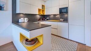 Una cocina moderna con armarios blancos, una encimera negra y un estante amarillo de acento.