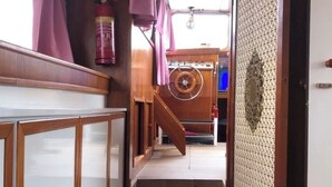 Un couloir étroit avec un escalier en bois menant à un niveau inférieur. Un meuble avec des portes en verre dépoli se trouve à gauche, et un panneau décoratif à droite.