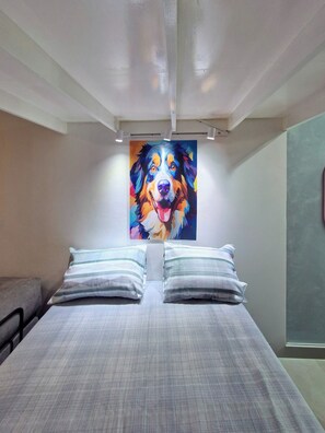 Un dormitorio con una cama grande, dos almohadas y un cuadro colorido de un perro en la pared.