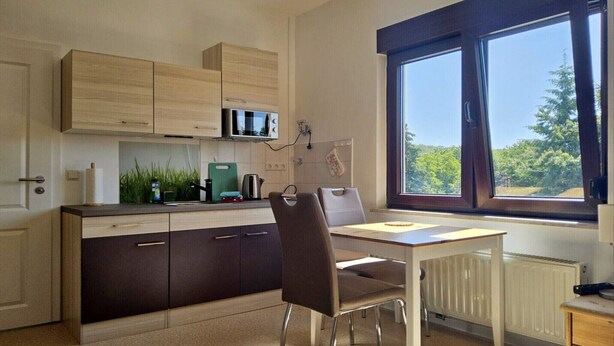 A compact kitchen with a dining area, a microwave, a kettle, and a window with a view of trees. - Haus Freigeist - zum Wanderer (Thale)