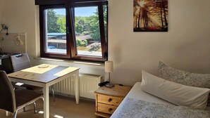 A room with a bed, a desk, a chair, a window with a view of greenery, and a painting on the wall. - Haus Freigeist - zum Wanderer (Thale)