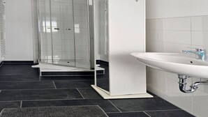 A modern bathroom with a glass-enclosed shower, a white pedestal sink, and dark tiled flooring. - Haus Freigeist - zum Wanderer (Thale)