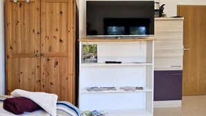 A bedroom with a wooden wardrobe, a TV on a white stand, and a bed with a striped blanket. - Haus Freigeist - zum Wanderer (Thale)