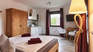 A hotel room with a bed, a wooden wardrobe, a desk with a chair, a television, and a window with curtains. - Haus Freigeist - zum Gartenblick (Thale)