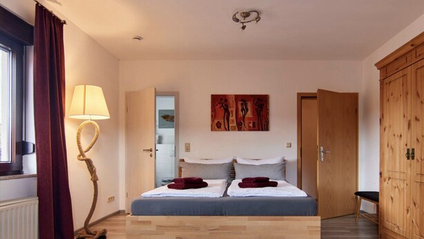 A bedroom with a wooden bed, a lamp, a wardrobe, and a painting on the wall. - Haus Freigeist - zum Gartenblick (Thale)