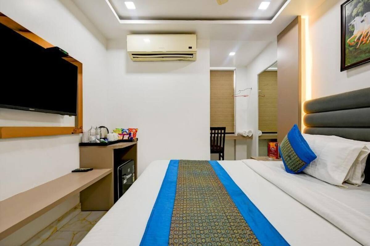 A hotel room with a bed, a desk with a computer, a flat-screen TV, an air conditioner, and a mirror.