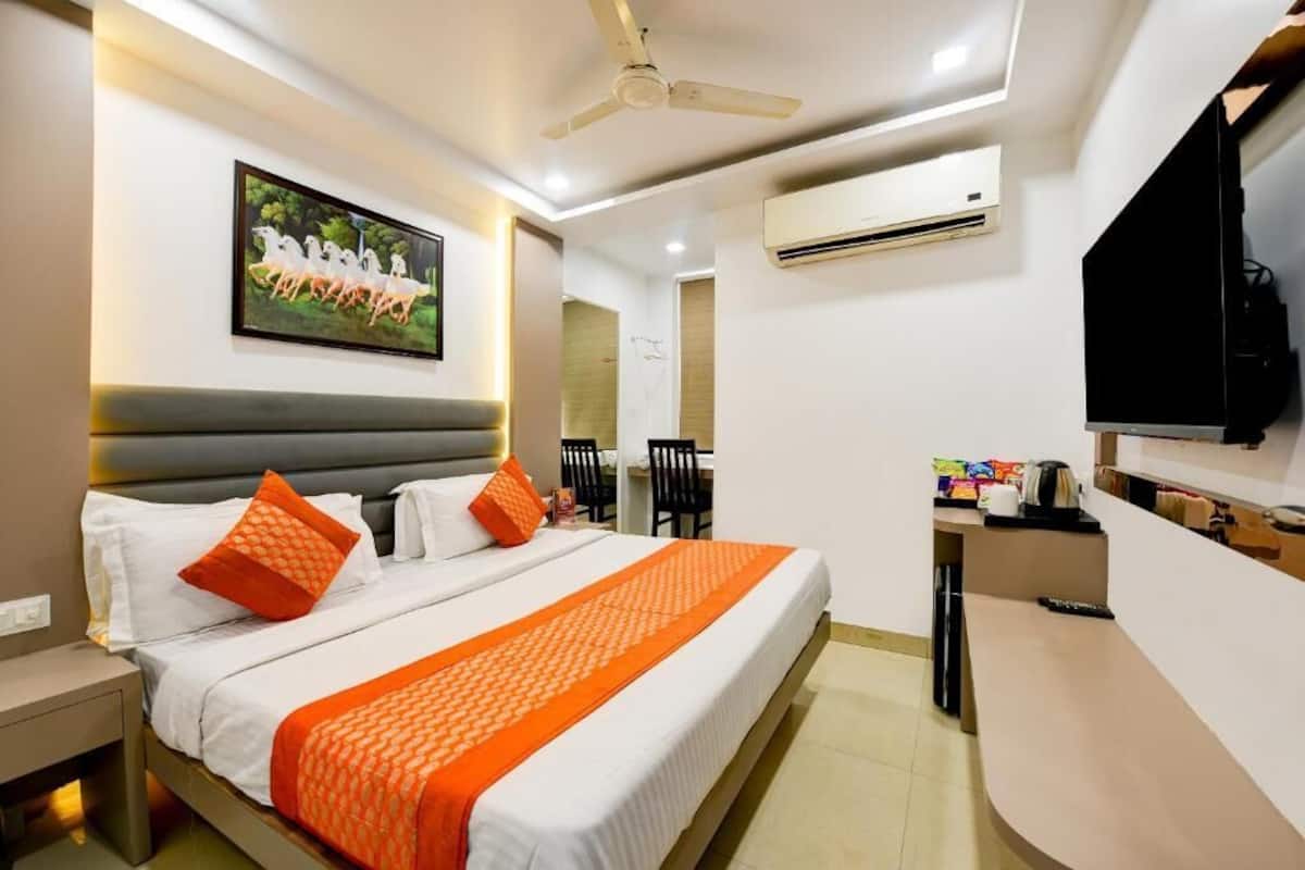 A hotel room with a bed, a desk, a chair, an air conditioner, and a television.