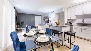 Un comedor moderno con una mesa de vidrio, sillas azules y platos blancos.