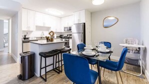Una cocina moderna con armarios blancos, una isla central y un comedor con sillas azules.
