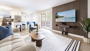 Una sala de estar moderna con un televisor de pantalla plana, un sofá, una mesa de centro y un comedor con una cocina al fondo.