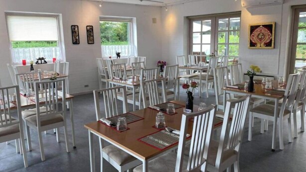 A dining area with white chairs and tables, large windows, and a wall-mounted artwork. - Marsktures motel (Højer)