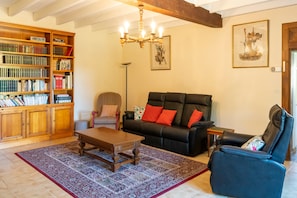 Ein Wohnzimmer mit Bücherregal, einer schwarzen Ledersofa, einem Holztisch und einem gemusterten Teppich.