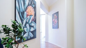 A hallway with wooden flooring, a potted plant, and two large abstract paintings on the walls.