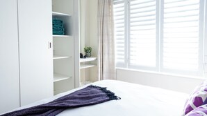 A bedroom with a bed, a wardrobe, a window with blinds, and a curtain.