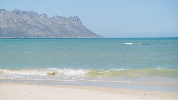 A beach with clear turquoise water and a mountain in the background.