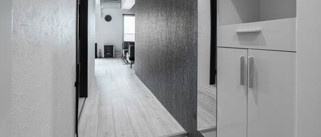 Un pasillo moderno con suelo de madera, pared texturizada oscura y un armario blanco con estante.