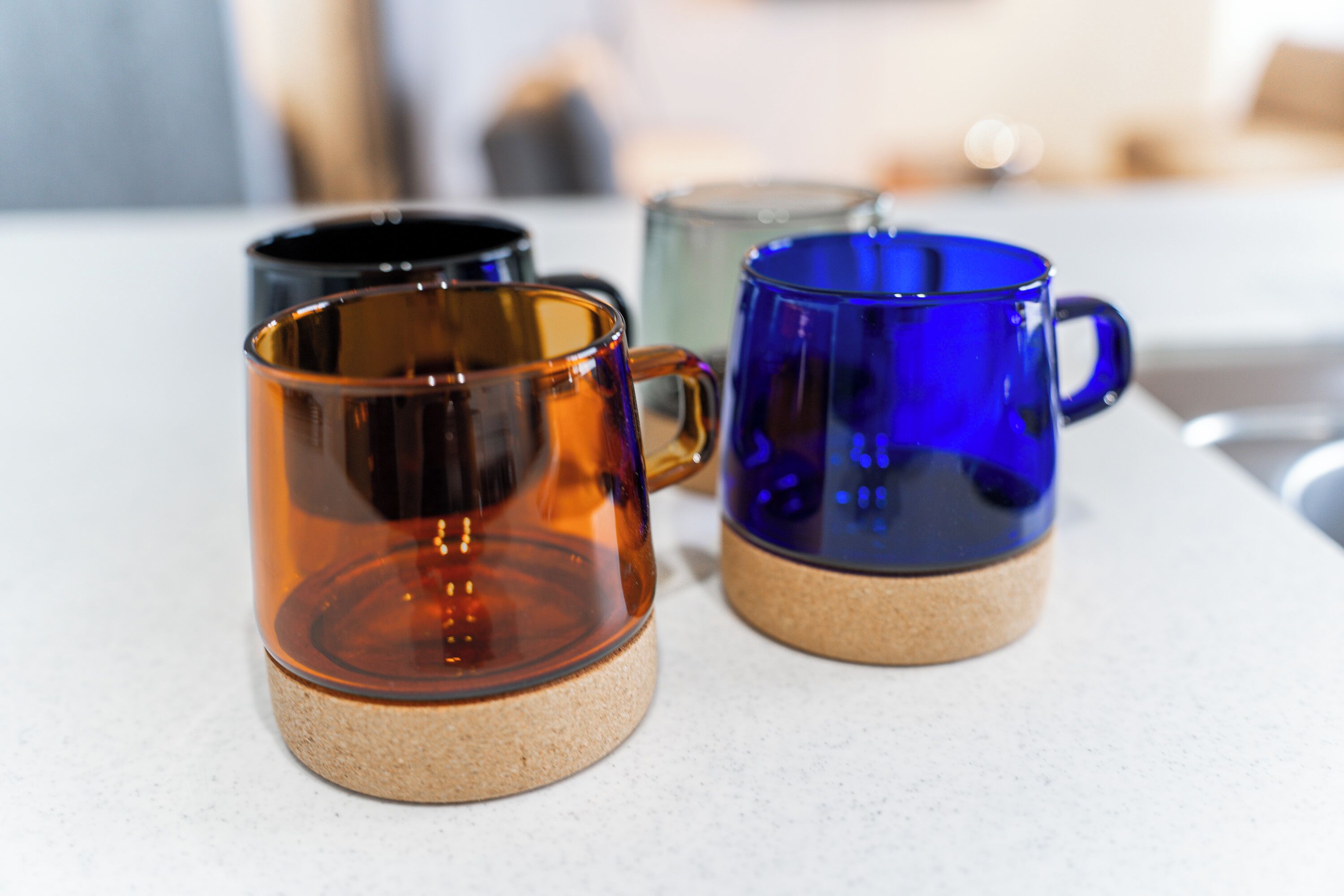 Three glass mugs with cork bases on a white countertop.