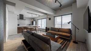 A modern living room with a sofa, coffee table, and a TV. There is a kitchen area with a dining table and chairs. - LUXIA 601 (Sapporo)