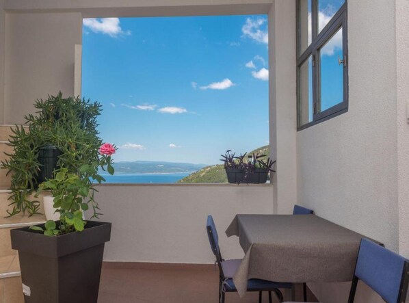 A balcony with a table and chairs, potted plants, and a view of the sea.