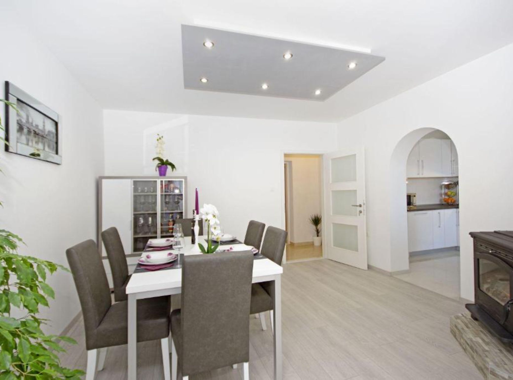 A dining area with a white table, four chairs, and a glass cabinet in the background.