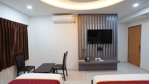 Habitación de hotel con dos camas, un televisor montado en un panel de madera, un escritorio con una silla y un equipo de aire acondicionado.