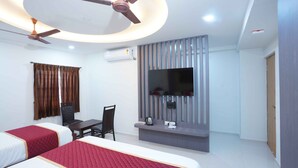Habitación de hotel con dos camas, un escritorio, una silla, un televisor montado en la pared y un ventilador de techo.