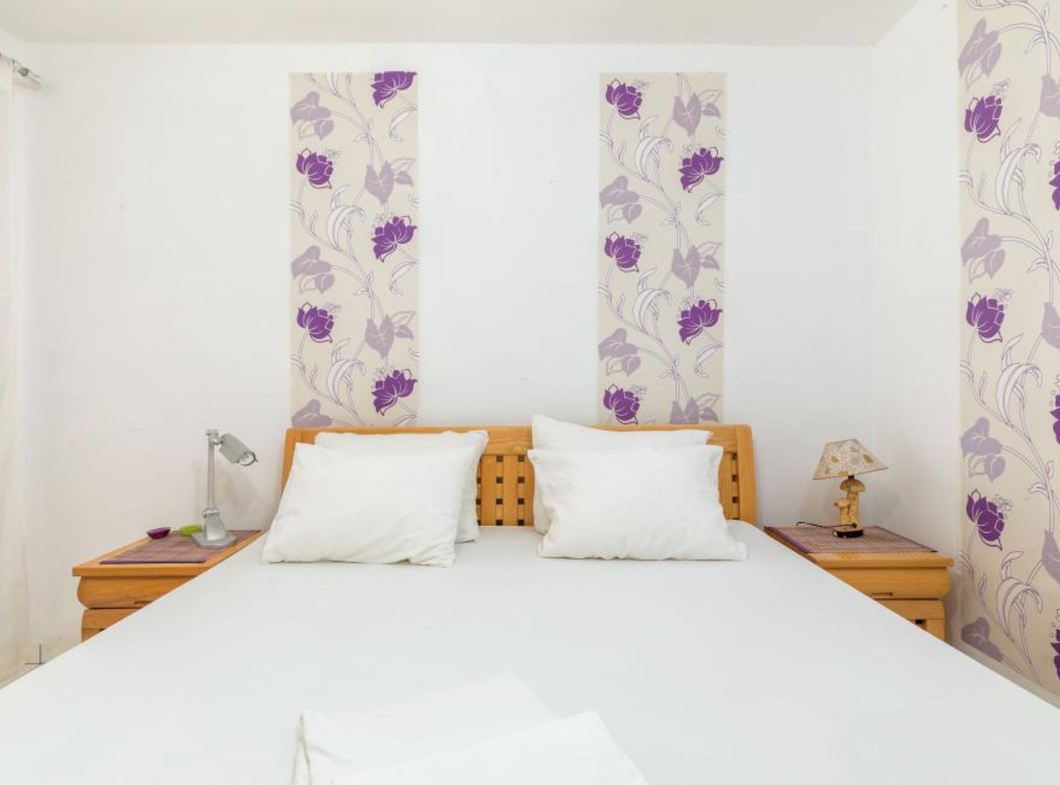 A bedroom with a bed, two pillows, a nightstand with a lamp, and a wall with floral wallpaper.