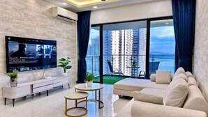 A modern living room with a flat-screen TV, a sofa, a coffee table, and a balcony with a city view. - Full Sea View Country Garden Danga Bay 11-13pax (Johor Bahru)