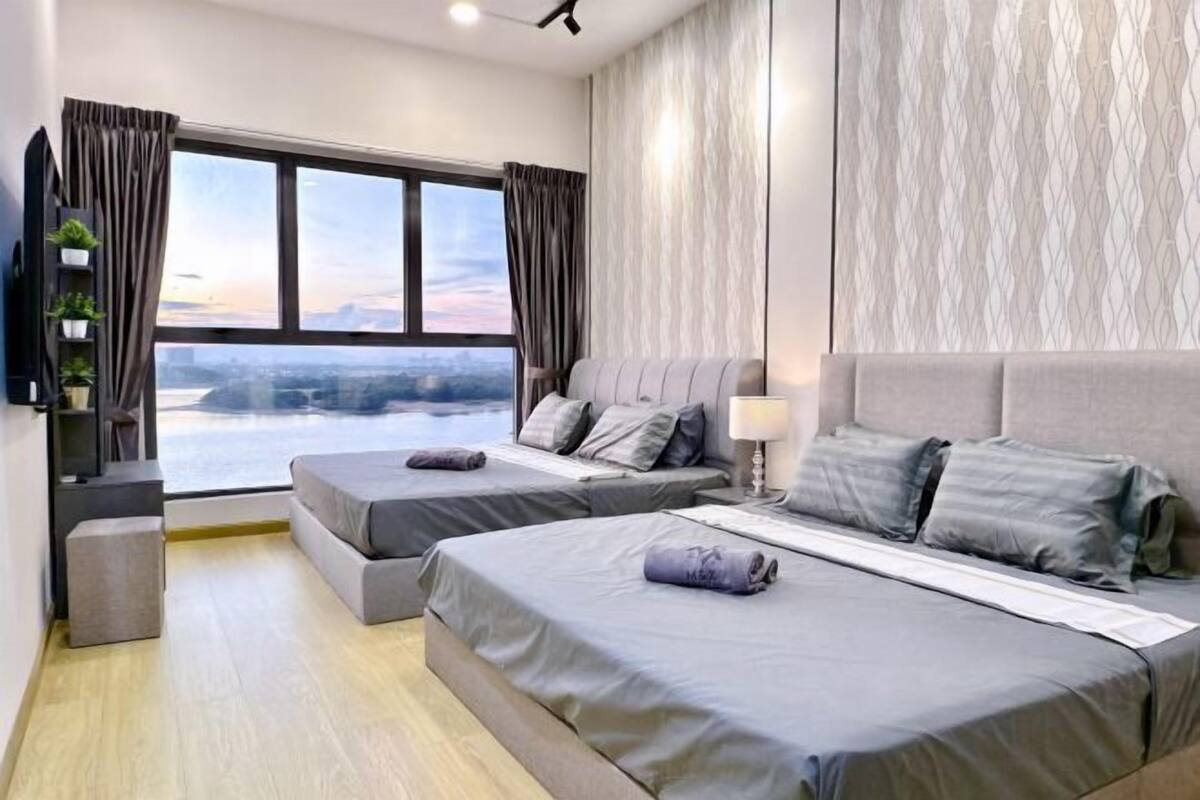 Ein modernes Hotelzimmer mit zwei Betten, einem großen Fenster mit Vorhängen, einem Flachbildfernseher und einer kleinen Pflanze auf einem Regal.