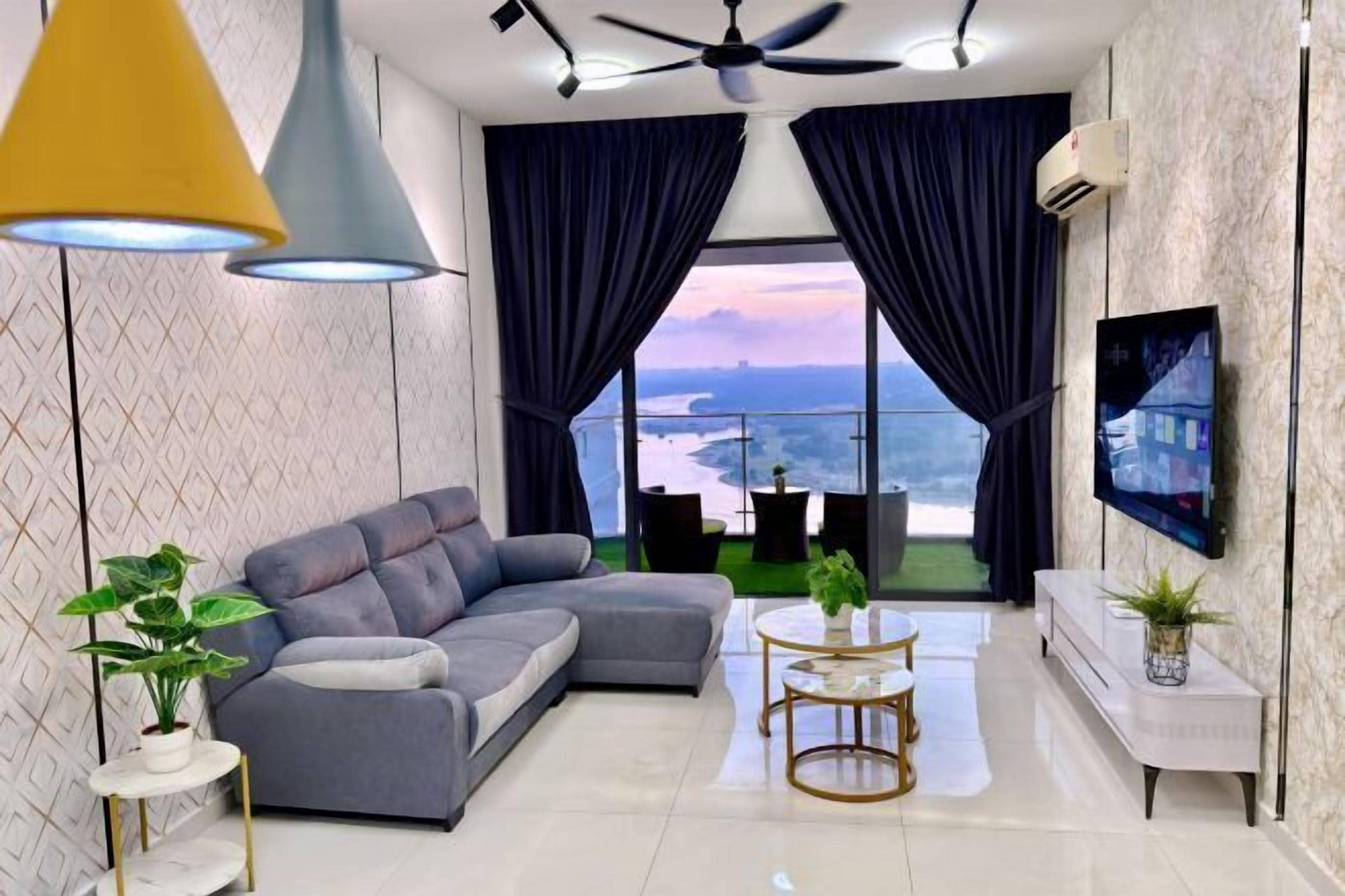 A modern living room with a sectional sofa, a round coffee table, a TV mounted on the wall, and a balcony with curtains.
