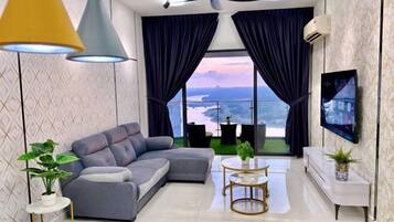 A modern living room with a sectional sofa, a round coffee table, a TV mounted on the wall, and a balcony with curtains.