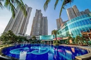 A swimming pool with a circular design, surrounded by tall residential buildings and palm trees.