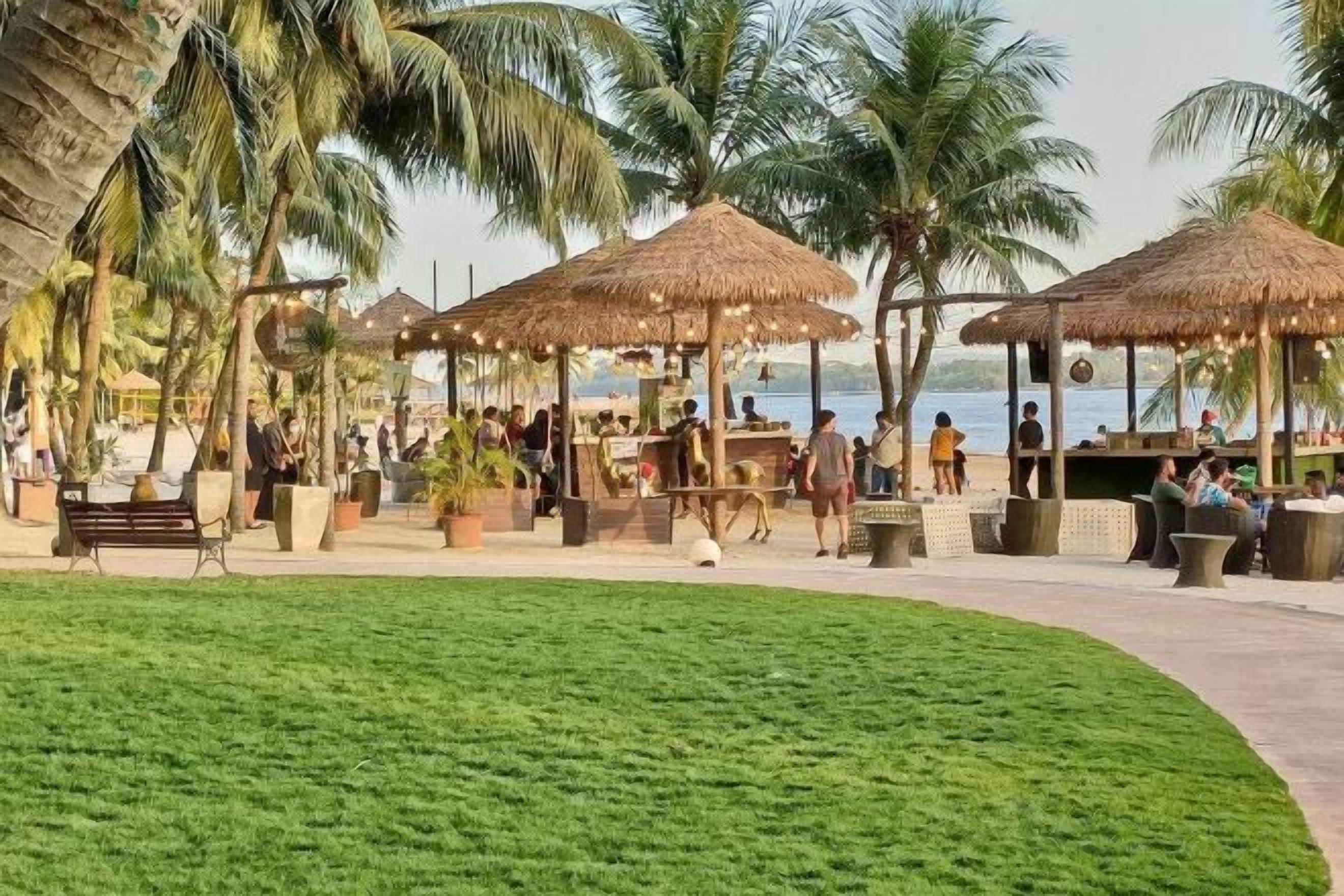 A tropical resort with thatched-roof structures, palm trees, and a grassy area.