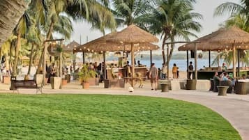 A tropical resort with thatched-roof structures, palm trees, and a grassy area.