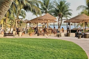 A tropical resort with thatched-roof structures, palm trees, and a grassy area.
