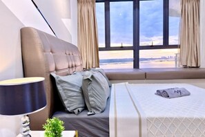 A hotel room with a bed, a nightstand, a lamp, and a view of the city through large windows.
