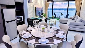 A modern dining area with a round table set for six, surrounded by chairs. There is a sofa and a balcony with a view of the water. - Full Sea View Country Garden Danga Bay 11-13pax (Johor Bahru)