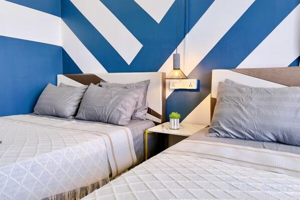 Habitación de hotel con dos camas, una mesita de noche y una lámpara fijada a la pared.