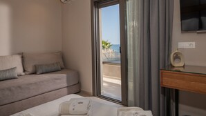 A hotel room with a sofa, a bed, a glass table, and a view of the sea through a sliding door.