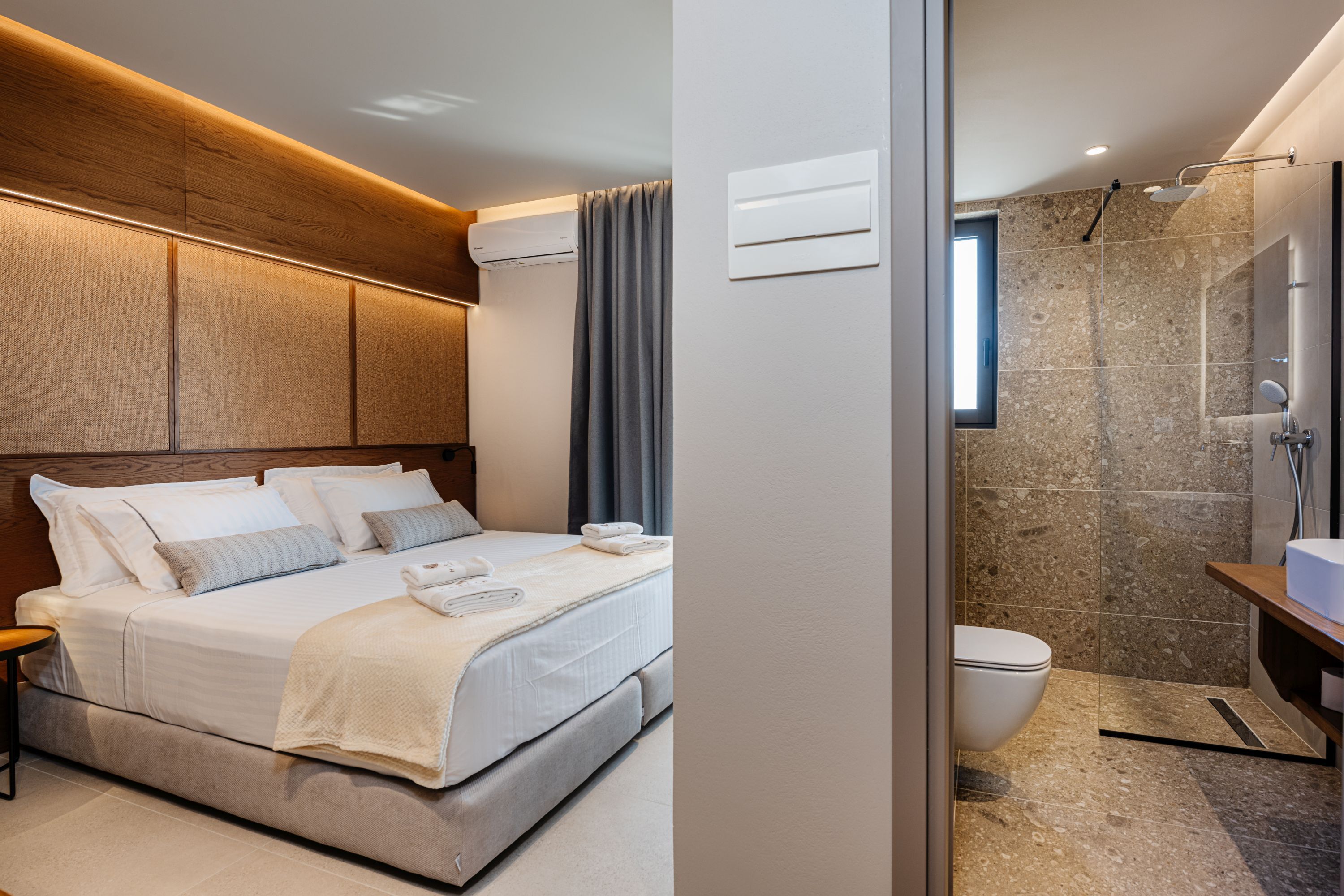 A modern hotel room with a large bed, a bedside table, a shower area, and a bathroom with a sink and toilet.