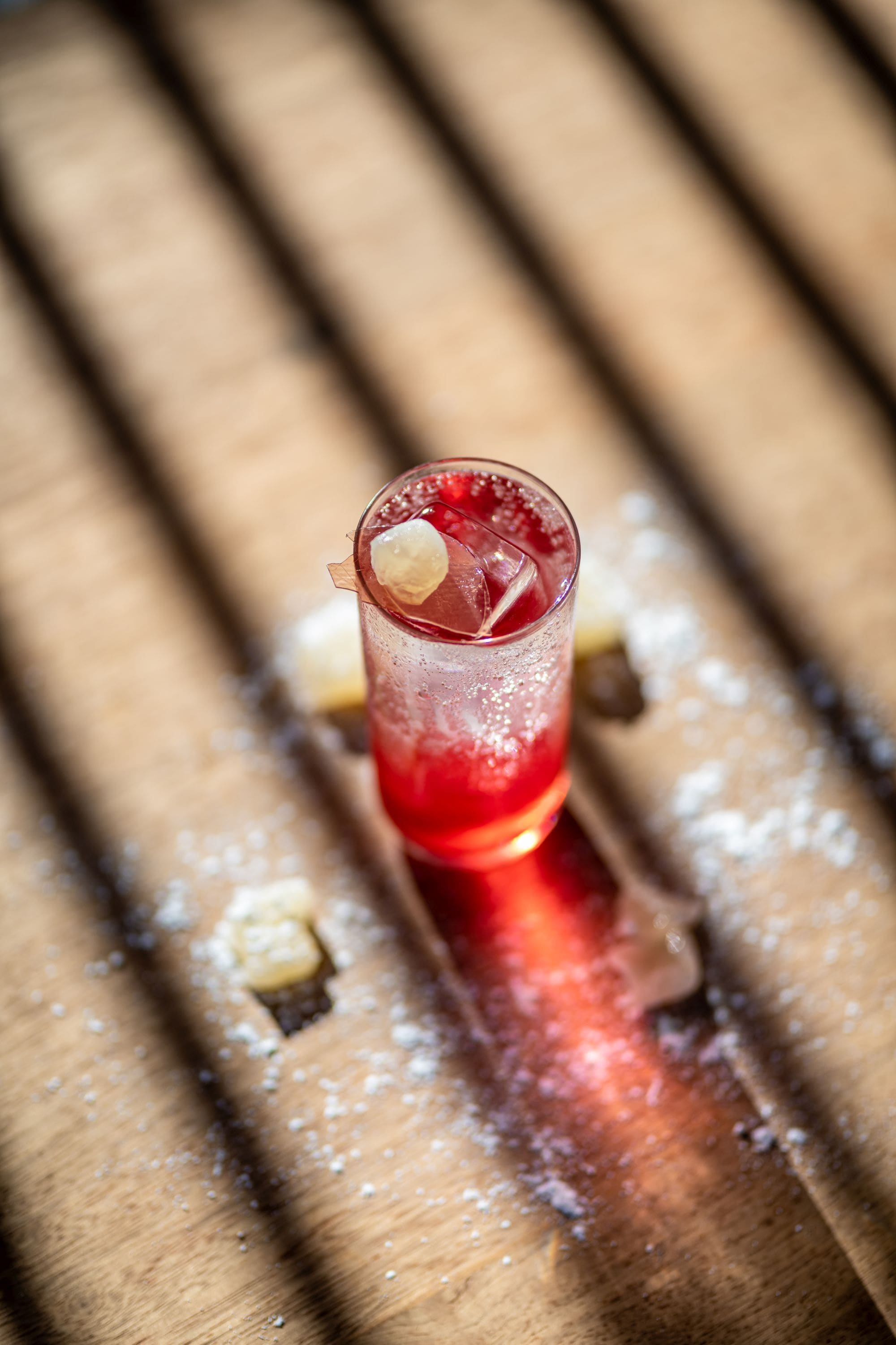 Gros plan d’un verre contenant une boisson rouge, des glaçons et une garniture, le tout posé sur une surface en bois.