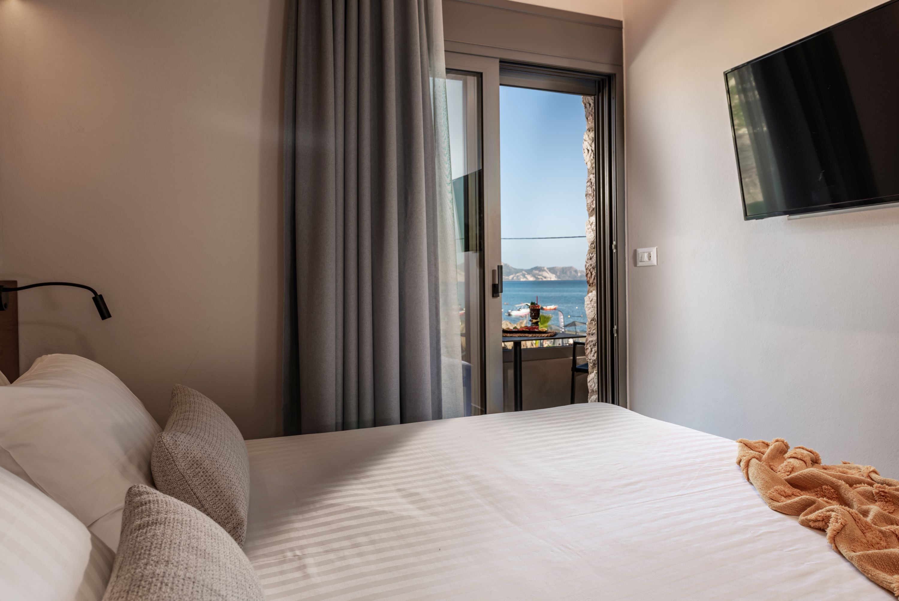 Habitación de hotel con cama, vista al mar y televisión en la pared.